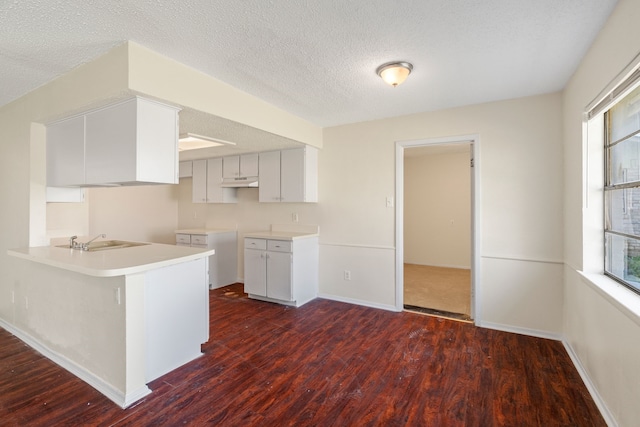 kitchen featuring kitchen peninsula, dark hardwood / wood-style flooring, a textured ceiling, sink, and white cabinetry