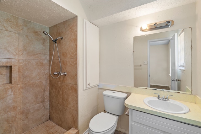 bathroom with tiled shower, vanity, a textured ceiling, and toilet