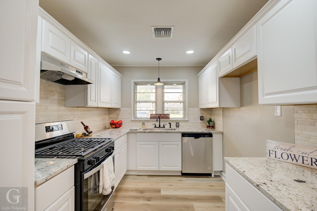 kitchen featuring stainless steel appliances, under cabinet range hood, a sink, light stone counters, and decorative backsplash