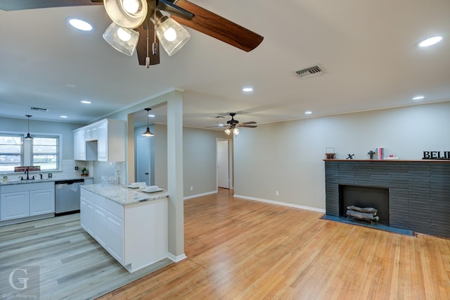 kitchen featuring a ceiling fan, dishwasher, a sink, white cabinets, and a fireplace