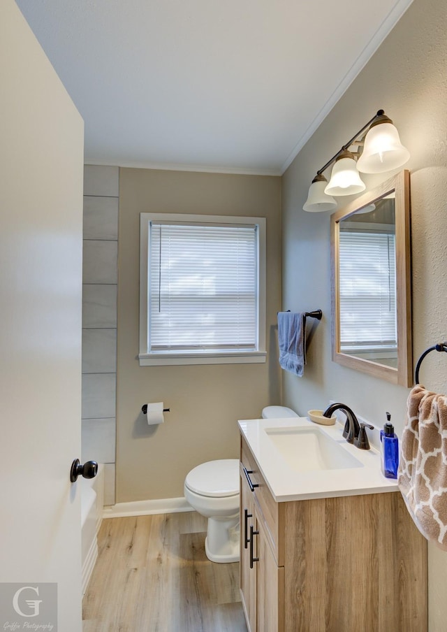 bathroom with wood finished floors, toilet, vanity, baseboards, and ornamental molding