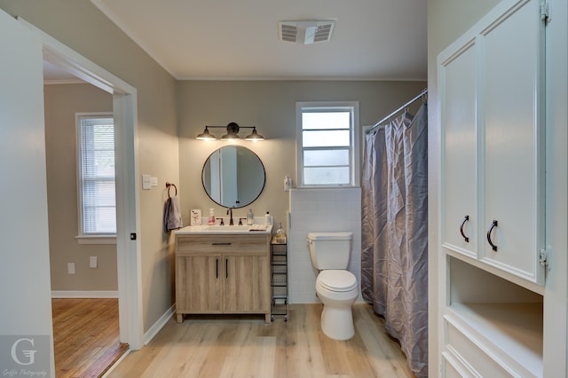 bathroom with wood finished floors, ornamental molding, toilet, vanity, and tile walls