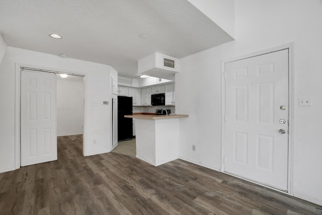 kitchen with black appliances, white cabinets, dark hardwood / wood-style floors, a textured ceiling, and kitchen peninsula