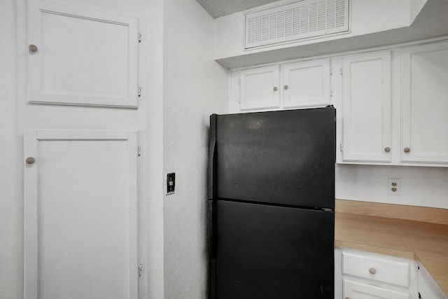 kitchen featuring black fridge, white cabinetry, a textured ceiling, and built in desk