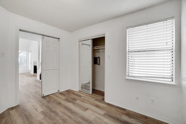 unfurnished bedroom featuring light hardwood / wood-style flooring, a barn door, multiple windows, and a closet