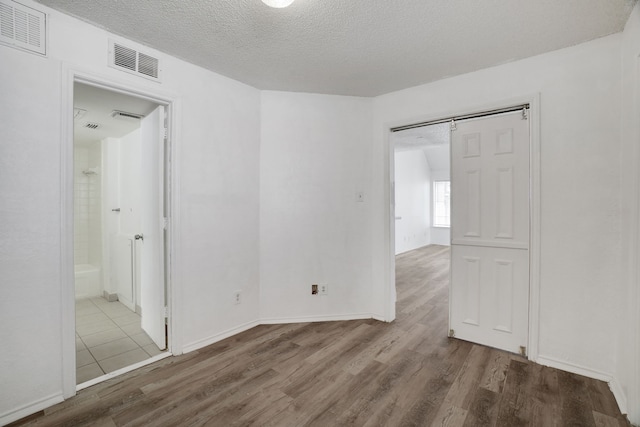 unfurnished room with hardwood / wood-style floors, a barn door, and a textured ceiling