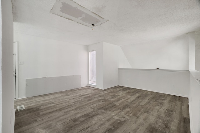 additional living space featuring a textured ceiling, dark hardwood / wood-style flooring, and vaulted ceiling