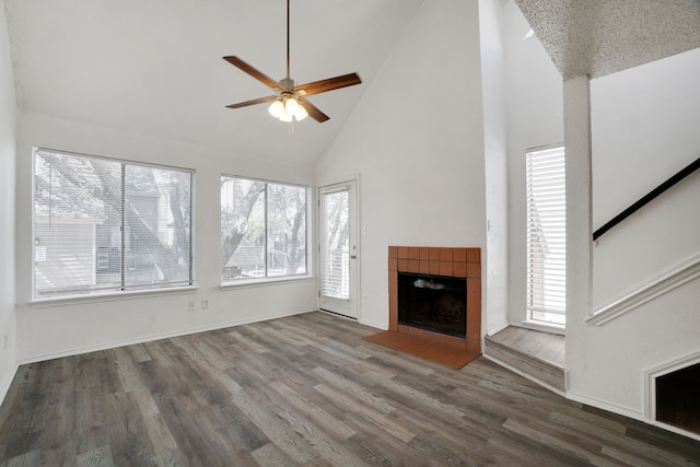 unfurnished living room with a tile fireplace, high vaulted ceiling, plenty of natural light, and dark wood-type flooring