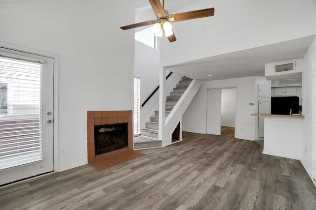 unfurnished living room featuring a tile fireplace, hardwood / wood-style floors, a towering ceiling, and ceiling fan