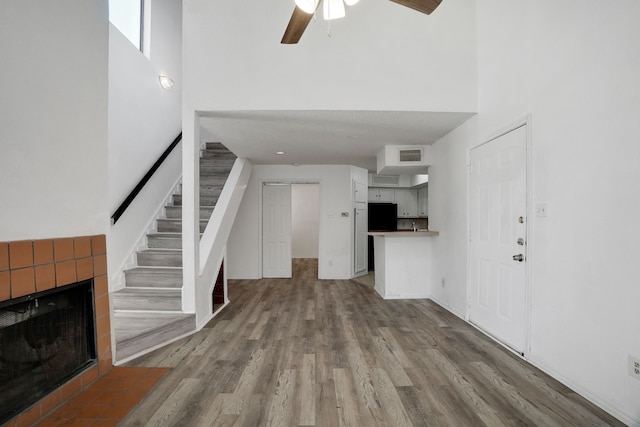 unfurnished living room featuring a fireplace, a high ceiling, light hardwood / wood-style flooring, and ceiling fan