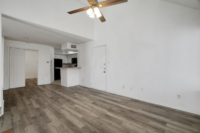 unfurnished living room featuring hardwood / wood-style flooring, ceiling fan, and a towering ceiling