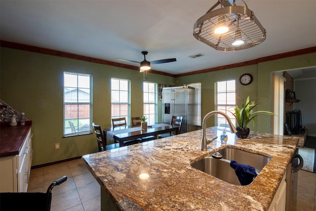 kitchen with dark stone counters, ceiling fan, crown molding, sink, and an island with sink