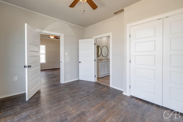 unfurnished bedroom with ceiling fan, ensuite bathroom, dark wood-type flooring, and a closet