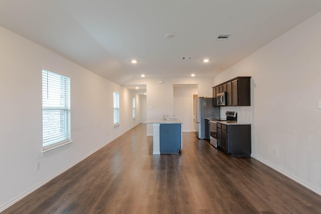 kitchen with sink, dark wood-type flooring, light stone counters, a kitchen island with sink, and appliances with stainless steel finishes