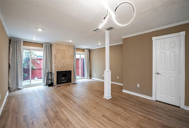 unfurnished living room featuring decorative columns, wood-type flooring, a large fireplace, ornamental molding, and a textured ceiling