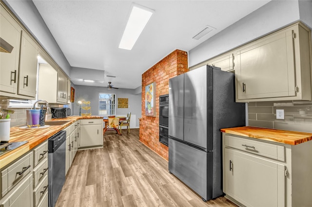 kitchen with appliances with stainless steel finishes, butcher block counters, sink, and light hardwood / wood-style flooring