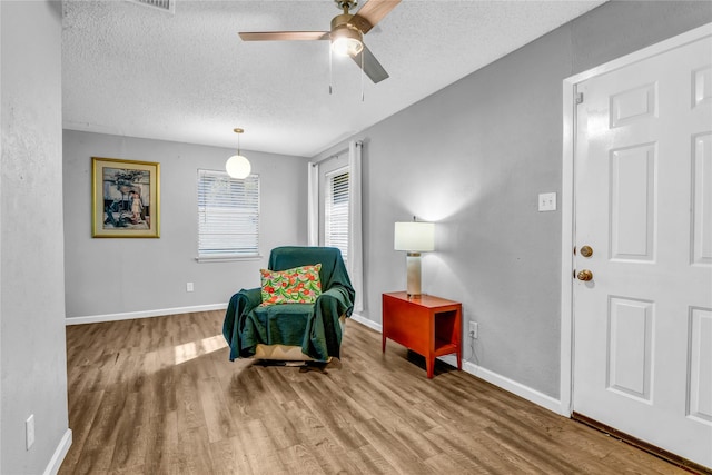 living area with ceiling fan, wood-type flooring, and a textured ceiling