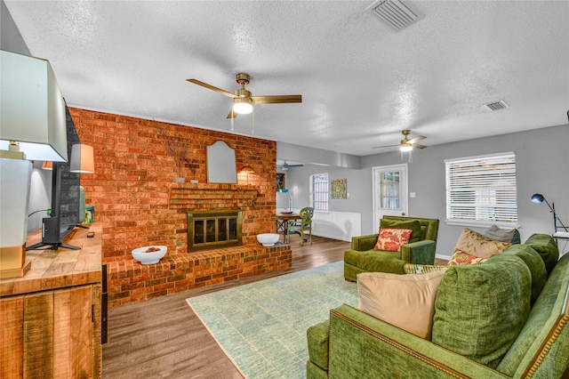 living room featuring ceiling fan, visible vents, a fireplace, and wood finished floors