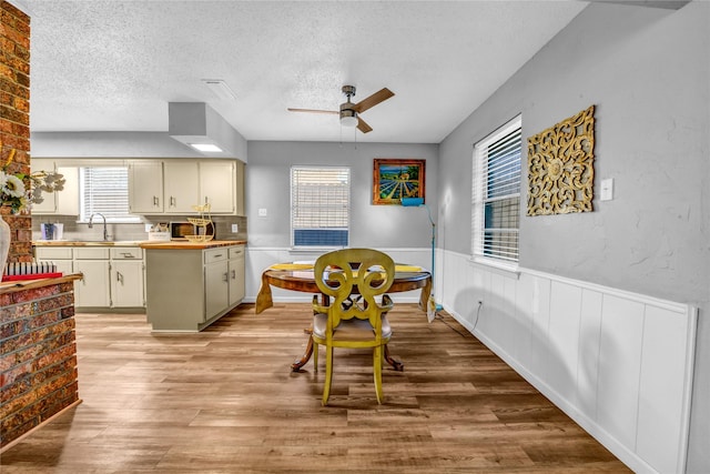 dining area featuring ceiling fan, light hardwood / wood-style floors, sink, and a textured ceiling