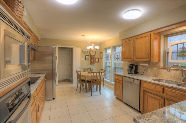 kitchen with light stone countertops, stainless steel appliances, sink, decorative light fixtures, and a notable chandelier