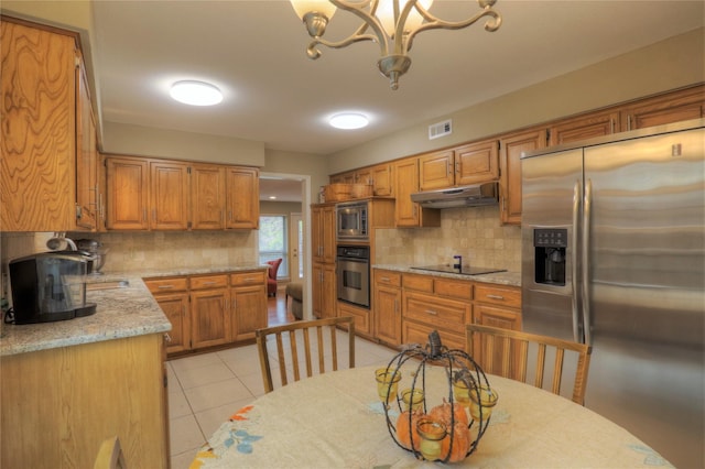 kitchen featuring light tile patterned floors, appliances with stainless steel finishes, tasteful backsplash, a notable chandelier, and light stone counters