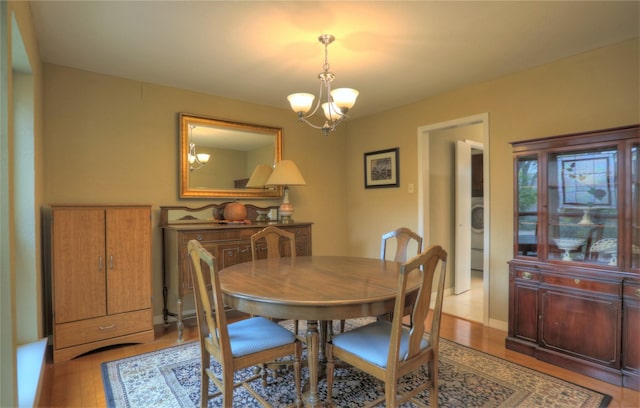 dining room featuring washer / dryer, light hardwood / wood-style flooring, and an inviting chandelier