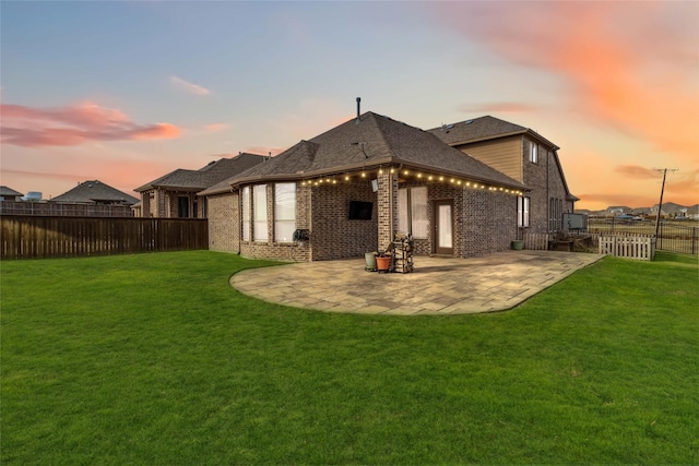 back house at dusk featuring a yard and a patio