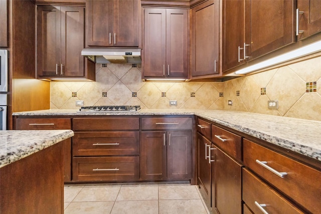 kitchen with light tile patterned floors, tasteful backsplash, light stone counters, and stainless steel gas stovetop