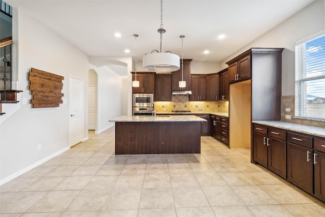 kitchen with backsplash, appliances with stainless steel finishes, decorative light fixtures, light stone counters, and dark brown cabinets