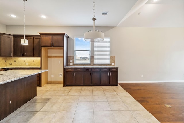 kitchen with dark brown cabinetry, light stone countertops, tasteful backsplash, decorative light fixtures, and light tile patterned floors