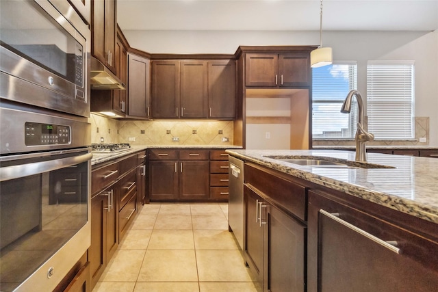 kitchen featuring hanging light fixtures, sink, light stone countertops, appliances with stainless steel finishes, and tasteful backsplash