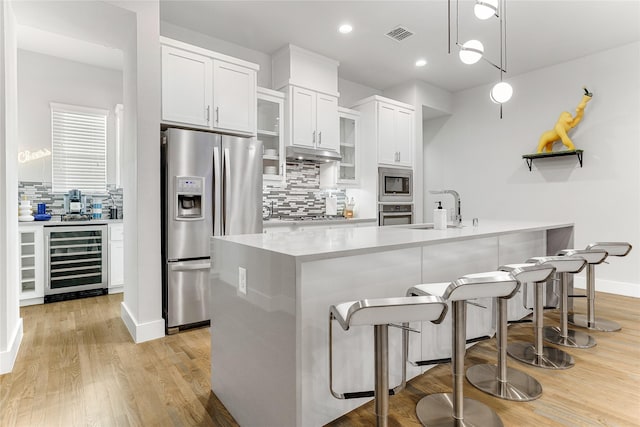 kitchen featuring white cabinetry, pendant lighting, stainless steel appliances, beverage cooler, and light hardwood / wood-style floors