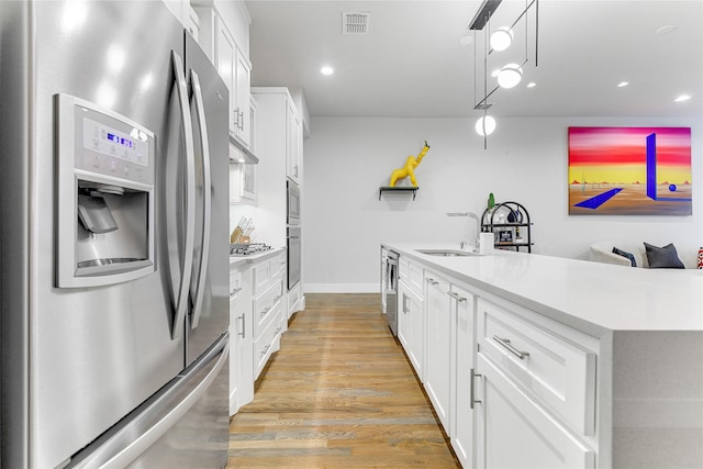 kitchen featuring sink, stainless steel appliances, decorative light fixtures, white cabinets, and light wood-type flooring