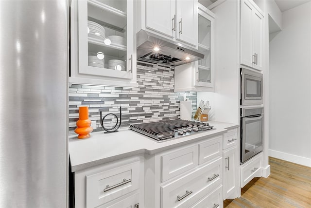 kitchen featuring decorative backsplash, white cabinets, stainless steel appliances, and light wood-type flooring