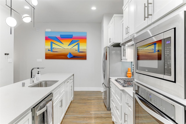 kitchen with sink, hanging light fixtures, light hardwood / wood-style floors, white cabinetry, and stainless steel appliances