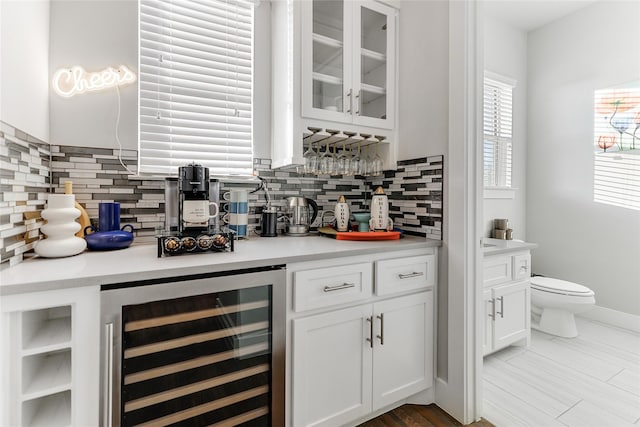 bar featuring backsplash, wine cooler, and white cabinetry