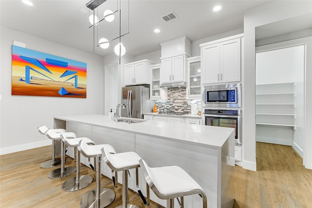 kitchen with tasteful backsplash, stainless steel appliances, decorative light fixtures, white cabinetry, and an island with sink