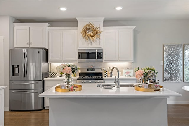 kitchen with appliances with stainless steel finishes, sink, white cabinets, decorative backsplash, and a center island with sink