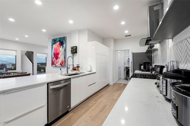 kitchen featuring sink, wall chimney exhaust hood, light hardwood / wood-style floors, white cabinetry, and stainless steel appliances