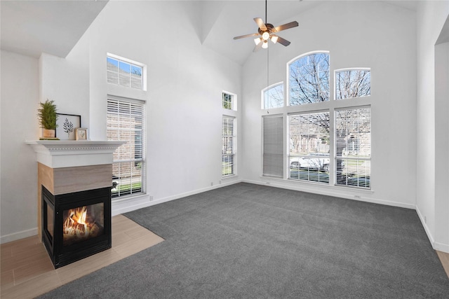 unfurnished living room with a multi sided fireplace, a high ceiling, ceiling fan, and carpet