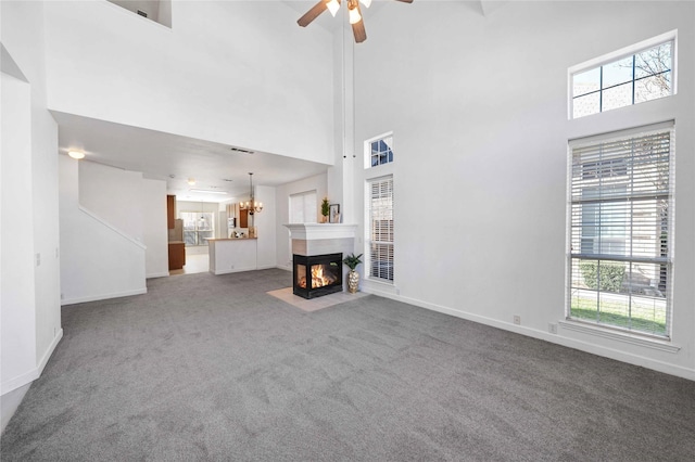 unfurnished living room featuring ceiling fan, a multi sided fireplace, carpet floors, and a high ceiling