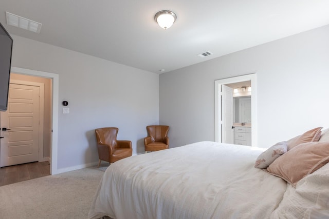 bedroom with ensuite bathroom and light colored carpet