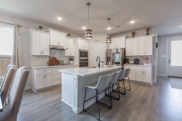 kitchen featuring decorative light fixtures, white cabinetry, an island with sink, and appliances with stainless steel finishes