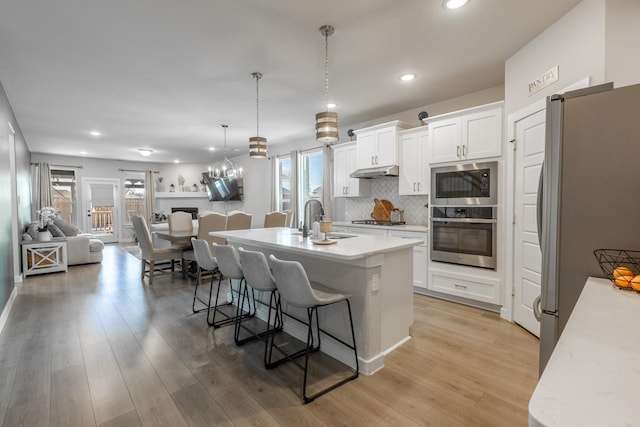 kitchen featuring a sink, under cabinet range hood, open floor plan, appliances with stainless steel finishes, and a breakfast bar area