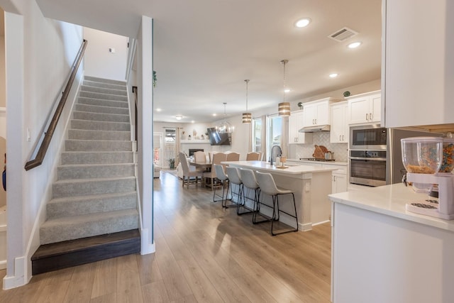 kitchen with stainless steel appliances, a kitchen island with sink, pendant lighting, white cabinetry, and a breakfast bar area