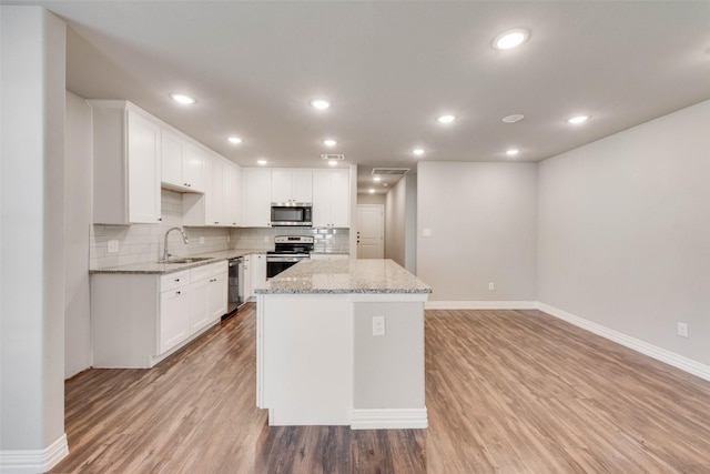 kitchen featuring white cabinetry, a center island, sink, stainless steel appliances, and light stone counters