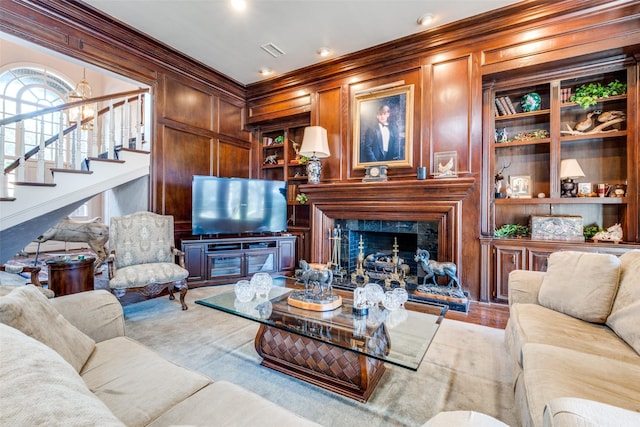 living room featuring wood walls, a fireplace, built in features, and ornamental molding