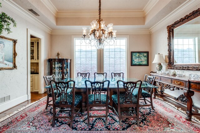 dining area featuring a raised ceiling, hardwood / wood-style flooring, ornamental molding, and a notable chandelier