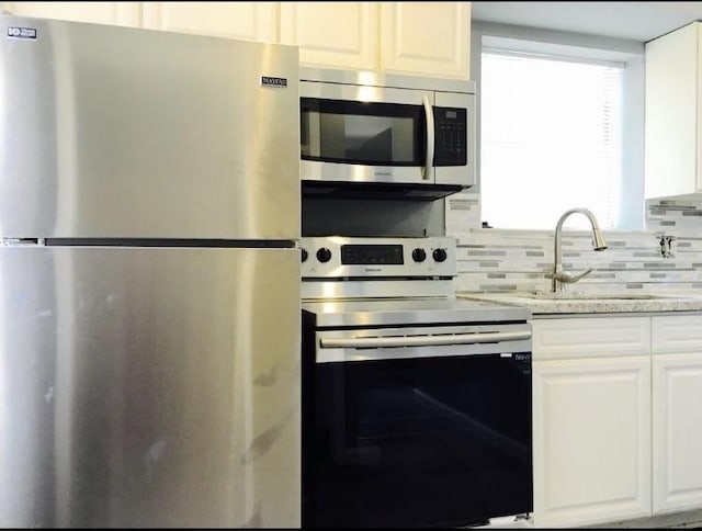 kitchen with light stone countertops, appliances with stainless steel finishes, tasteful backsplash, sink, and white cabinetry