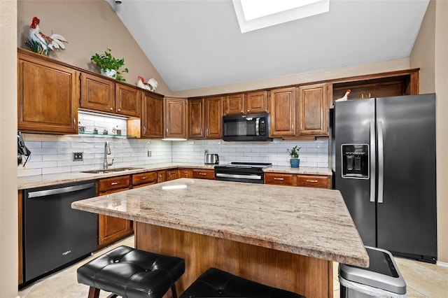 kitchen featuring black appliances, a kitchen breakfast bar, sink, vaulted ceiling with skylight, and tasteful backsplash